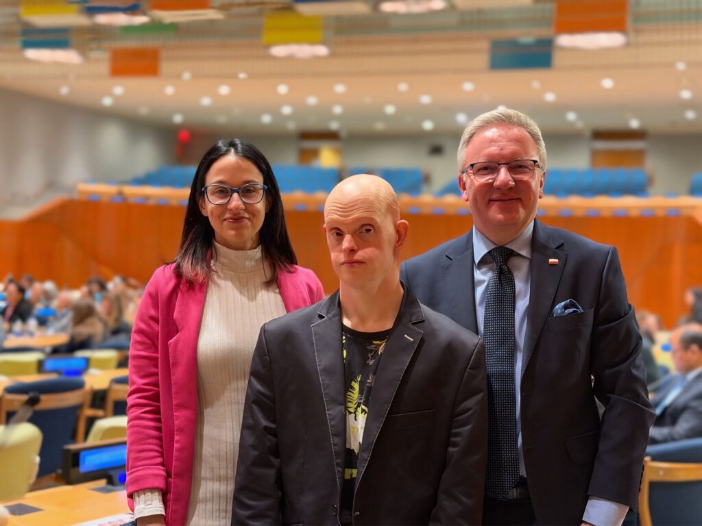 Od lewej: Marta Domańska, Michał Milka i ambasador Krzysztof Szczerski, w eleganckim ubiorze. W tle: sala plenarna Zgromadzenia Ogólnego ONZ