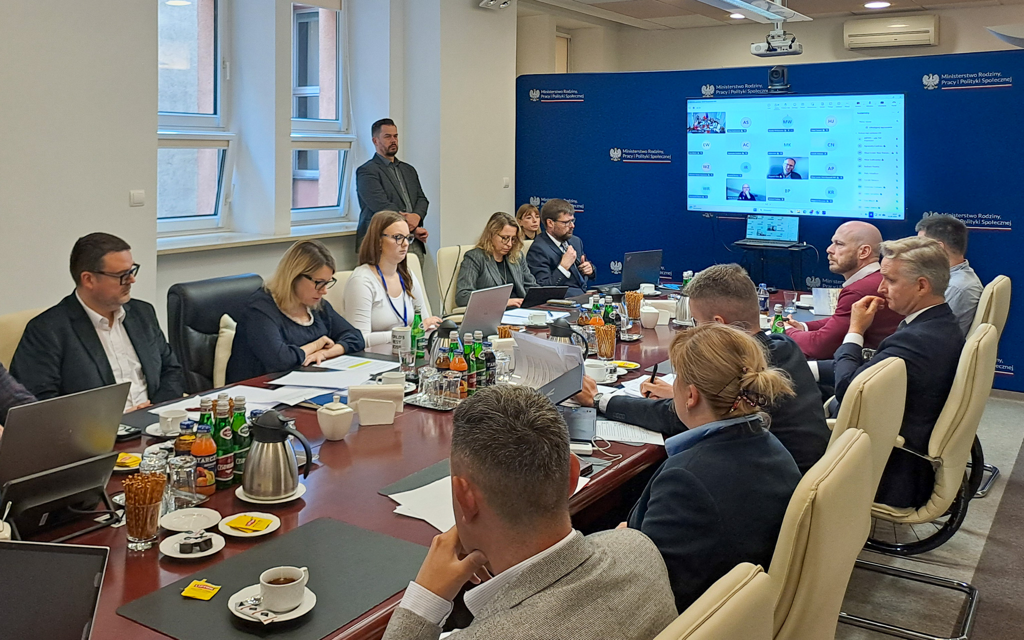 Posiedzenie Krajowej Rady Konsultacyjnej do Spraw Osób Niepełnosprawnych w siedzibie MRPiPS. Uczestnicy siedzą przy stole konferencyjnym, część osób bierze udział w spotkaniu zdalnie. Wśród uczestników są Pełnomocniczka Rządu ds. Osób Niepełnosprawnych Monika Sikora i dyrektor BON Krzysztof Czechowski.