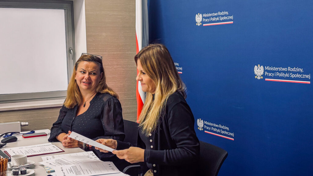 Rada Programowa Centrum Komunikacji rozpoczęła działalność 2 Dwie uczestniczki posiedzenia Rady Programowej Centrum Komunikacji rozmawiają przy stole konferencyjnym. Przed nimi leżą dokumenty związane z posiedzeniem, w tle ścianka MRPiPS.