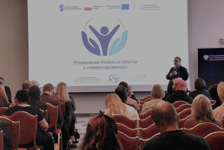 Zdjęcie przedstawia salę konferencyjną, w której trwa prezentacja. Na dużym ekranie widoczny jest slajd z napisem „Przebudowa modelu orzekania o niepełnosprawności” oraz logotypami instytucji i projektu. Przed ekranem stoi Dyrektor Biura Pełnomocnika Rządu do Spraw Osób Niepełnosprawnych trzymający mikrofon i prowadzący wystąpienie. Na pierwszym planie siedzą uczestnicy spotkania zwróceni w stronę prelegenta.